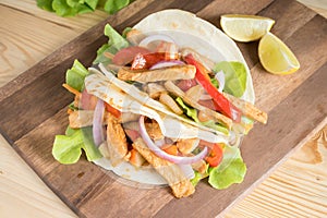 Grilled meat with onion and bell peppers, tomato,lettuce and serve with flour tortilla on wooden board.