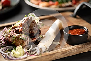 Grilled meat pieces, shish kebab with onion served on wooden board with ketchup.