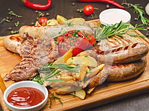 Grilled meat platter with pork and chicken steak, sausages and peasant potatoes with two sauces