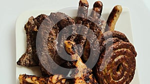 Grilled meat platter. Round sausage, chicken thighs, beef steak on a white plate close-up.Fried meat products. BBQ