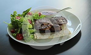 Grilled meat served with greens and pitta bread on white plate at the restaurant