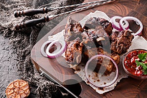 Grilled meat or shish kebab, shashlik with tomato sauce on wooden board over dark stone background. Top view