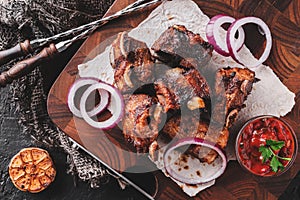 Grilled meat or shish kebab, shashlik with tomato sauce on wooden board over dark stone background. Top view