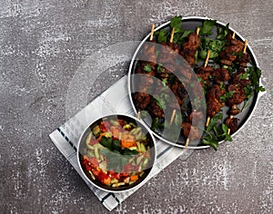 Grilled meat - shish kebabs on a wooden skewers on a round plate served with fresh vegetable salad on a dark background