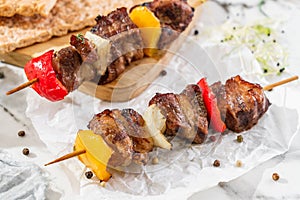 Grilled meat shish on skewers with vegetables on paper over light table. Healthy food. Hot meat dishes, shashlik food, closeup