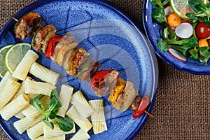 Grilled meat skewers with pasta on plate with vegetable sal