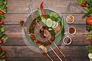 Grilled meat skewers in round plate surrounded by Sichuan pepper, Chinese spices and vegetable on wooden table