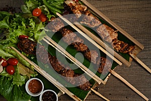 Grilled meat skewers served in bamboo barrel plate with Chinese spices and vegetable on rustic wooden table