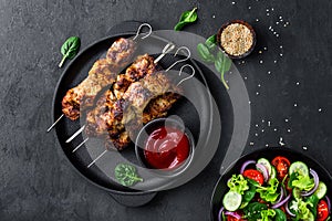 Grilled meat skewers, shish kebab and healthy vegetable salad of fresh tomato, cucumber, onion, spinach, lettuce and sesame on bla