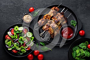 Grilled meat skewers, shish kebab and healthy vegetable salad of fresh tomato, cucumber, onion, spinach, lettuce and sesame on bla