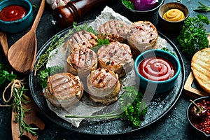 Grilled medallions wrapped in bacon. in a pan, ready to eat. On a black concrete background.