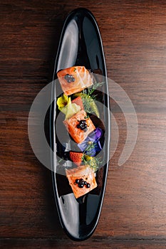 Grilled Medium Rare Salmon Cube topping with caviar and served with strawberry and orange in black plate