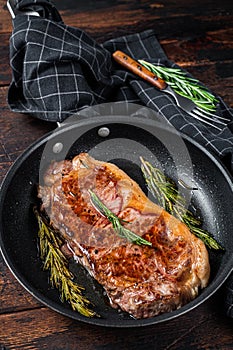 Grilled new york strip beef meat steak in a pan with herbs. Dark wooden background. Top view