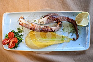 Grilled octopus on a blue plate with vegetables in restaurant in Greece