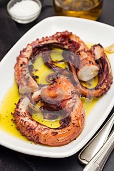 Grilled octopus with garlic on white dish on black background