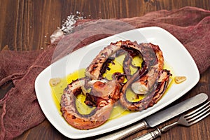 Grilled octopus with garlic on white dish on wooden background