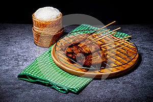 Grilled pork on bamboo skewers placed on a steel grill in a wooden tray with sticky rice in the cart, ready to serve