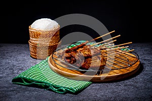 Grilled pork on bamboo skewers placed on a steel grill in a wooden tray with sticky rice in the cart, ready to serve