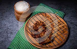 Grilled pork on bamboo skewers placed on a steel grill in a wooden tray with sticky rice in the cart, ready to serve