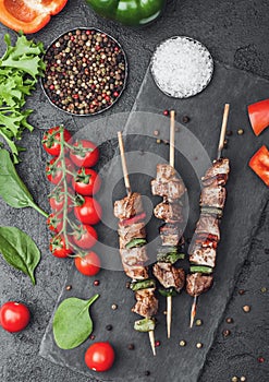 Grilled pork and chicken kebab with paprika on stone chopping board with salt, pepper and tomatoes on black background. Fresh