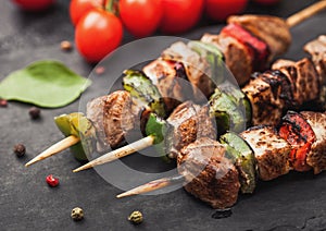 Grilled pork and chicken kebab with paprika on stone chopping board with salt, pepper and tomatoes on black background