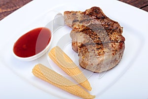 Grilled pork chop with Cranberry sauce and Mini Corn cob preserved on plate on wooden board