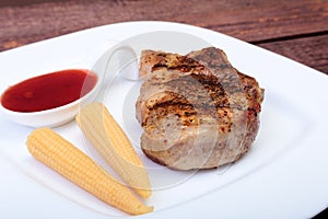 Grilled pork chop with Cranberry sauce and Mini Corn cob preserved on plate on wooden board