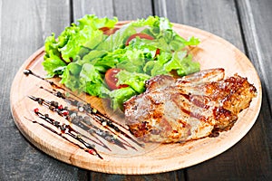 Grilled pork chop steak with fresh vegetable salad, tomatoes and sauce on wooden cutting board. Hot Meat Dishes