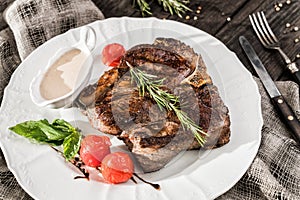 Grilled pork chop steak with rosemary, tomatoes and spices on wooden rustic background. Hot Meat Dishes.