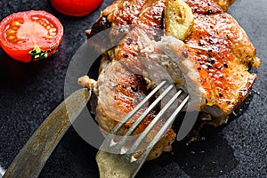 Grilled pork chop with tomatoes top view with knife and slice on fork over black Dish close up