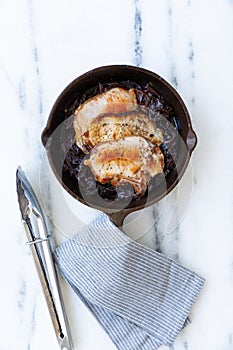 Grilled pork chops with red onion sauce on a cast iron skillet, with stripped napkin and kitchen clamps