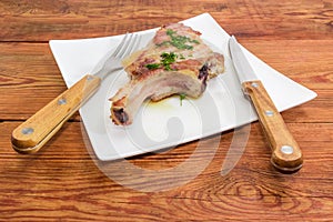 Grilled pork loin on bone on dish, fork and knife