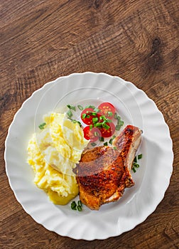 Grilled pork loin with mashed potatoes and salad in white plate on wooden table background with copy space. top view