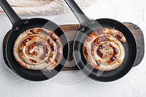 Grilled pork meat sausages in cast iron frying pan, on white background, top view flat lay