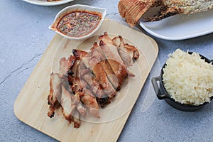 Grilled pork neck with dipping spice sauce and sticky rice on white table.