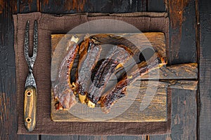 Grilled pork rib, on wooden serving board, with barbeque knife and meat fork, on old dark  wooden table background, top view flat