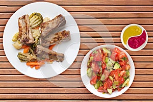 Grilled pork ribs with broccoli cabbage, carrots and garlic on a white plate. fried pork ribs with vegetables on a wooden