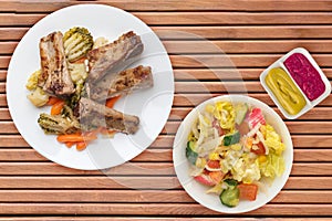 Grilled pork ribs with broccoli cabbage, carrots and garlic on a white plate. fried pork ribs with vegetables on a wooden