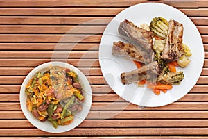 Grilled pork ribs with broccoli cabbage, carrots and garlic on a white plate. fried pork ribs with vegetables on a wooden