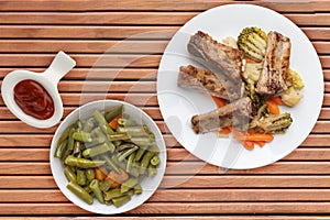 Grilled pork ribs with broccoli cabbage, carrots and garlic on a white plate. fried pork ribs with vegetables on a wooden