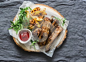 Grilled pork ribs and french fries on wooden board on grey background, top view. Delicious appetizers, tapas