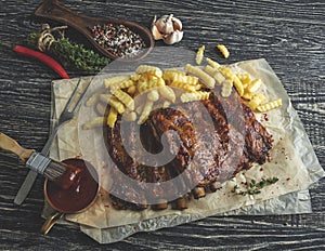 Grilled pork ribs with sauce on a cutting board, french fries, spices, wooden background