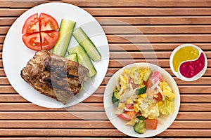 Grilled pork ribs with sliced cucumbers and tomatoes on a white plate. pork ribs on wooden background