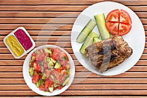 Grilled pork ribs with sliced cucumbers and tomatoes on a white plate. pork ribs on wooden background