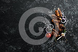 Grilled pork ribs with spices on black stone background.