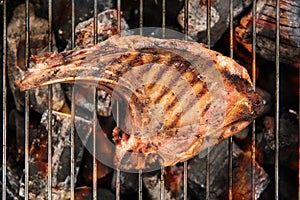 Grilled pork steaks over flames on the grill.