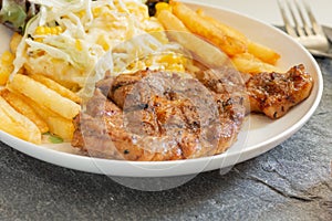 Grilled pork steaks on white plate with salad and french fries and ketchup on stone background