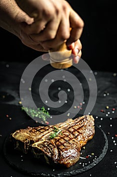 Grilled Porterhouse steak. Chef season salt on a juicy beef steak in a restaurant. in a freeze motion. American meat restaurant.