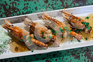 Grilled prawns sold at a street food market stall on a plate with sauce and herbs. Chinatown, Bangkok, Thailand