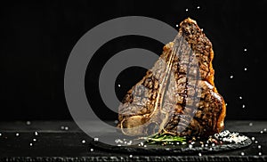 Grilled Premium Dry Aged T-bone Steak or porterhouse steak adding salt in a freeze motion on black background. USDA Prime Beef.